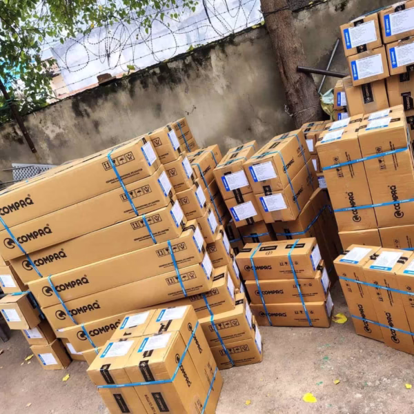 Stacked boxes of Voltmen energy storage batteries, ready for installation or distribution, situated outdoors against a concrete wall with barbed wire fence.